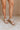 Front side view of female model wearing the Sofft Camille Sandal in Tapioca Grey which features light grey upper fabric, Side zipper with matching leather pull, cross straps and stacked block heel