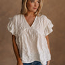 Upper body front view of female model wearing the Vivienne White Textured Top that has white textured fabric, short ruffled sleeves, and v neckline. worn with jeans.
