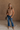 Full body front view of female model wearing the Nora Smocked Lettuce Hem Short Sleeve Top in tan that has stretchy textured fabric, lettuce trim, short sleeves, and a cropped fit.