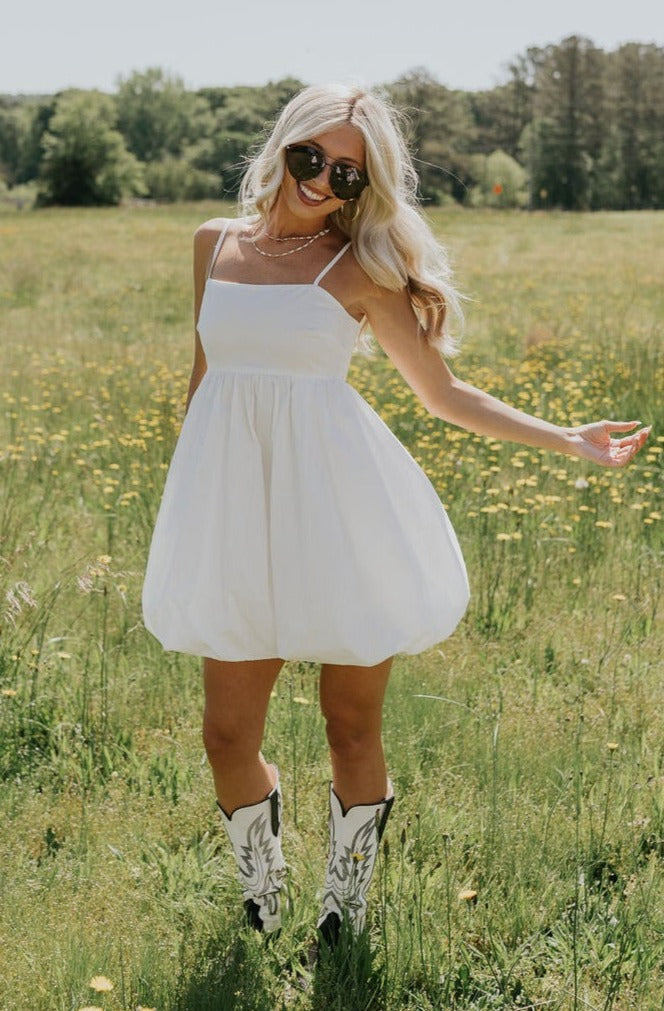 Full body front view of female model wearing the Rosemary White Bubble Hem Mini Dress that has white fabric, a bubble hem, and thin straps.
