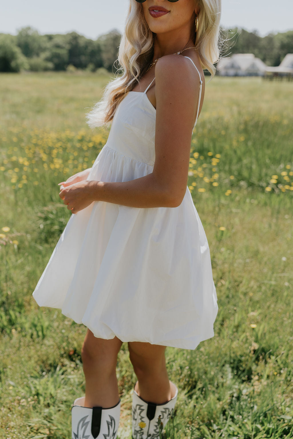 Side view of female model wearing the Rosemary White Bubble Hem Mini Dress that has white fabric, a bubble hem, and thin straps.