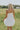 Back view of female model wearing the Rosemary White Bubble Hem Mini Dress that has white fabric, a bubble hem, and thin straps.