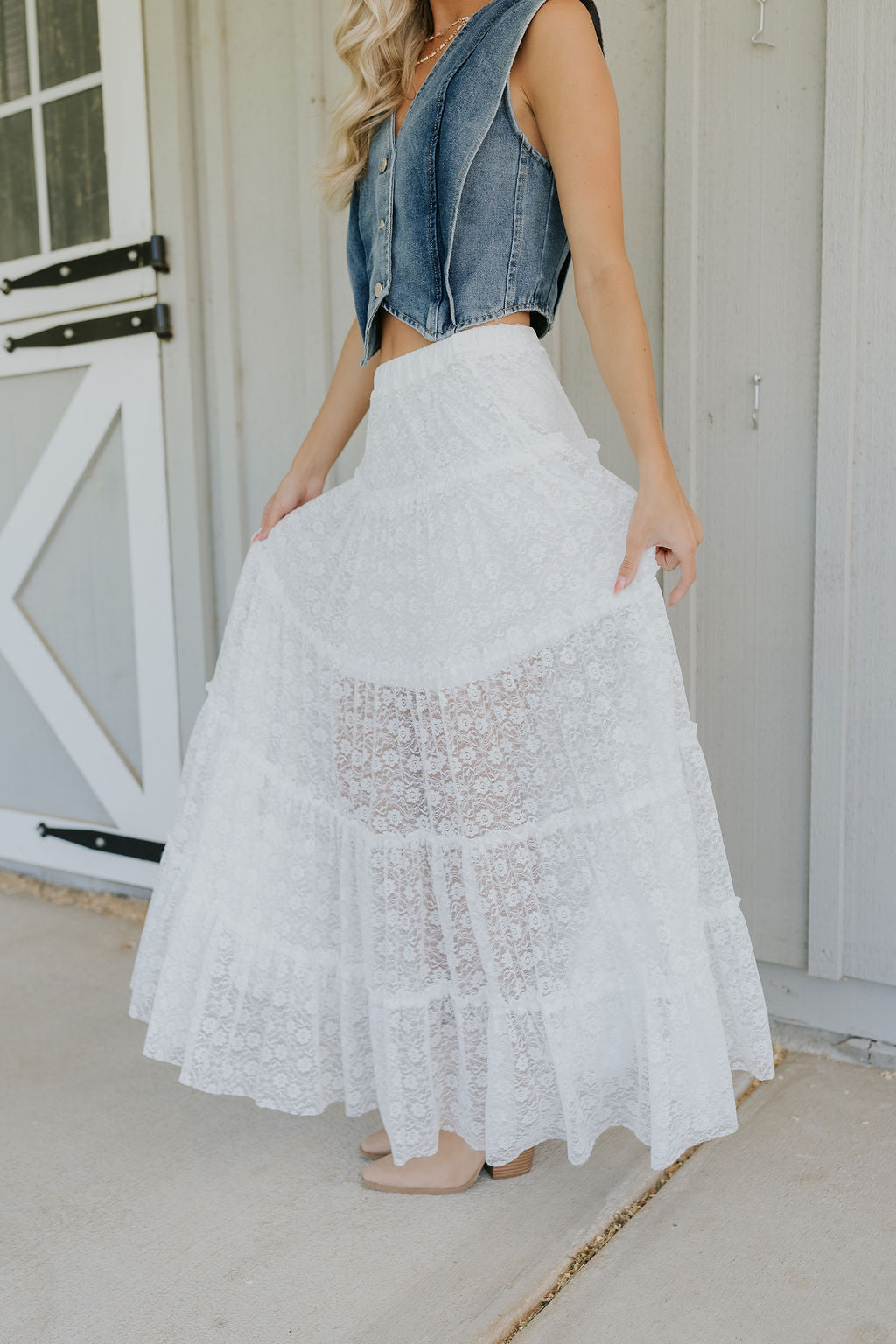 Lower body side view of female model wearing the Shiloh White Lace Maxi Skirt that has white lace fabric, half lining, and an elastic waist. 
