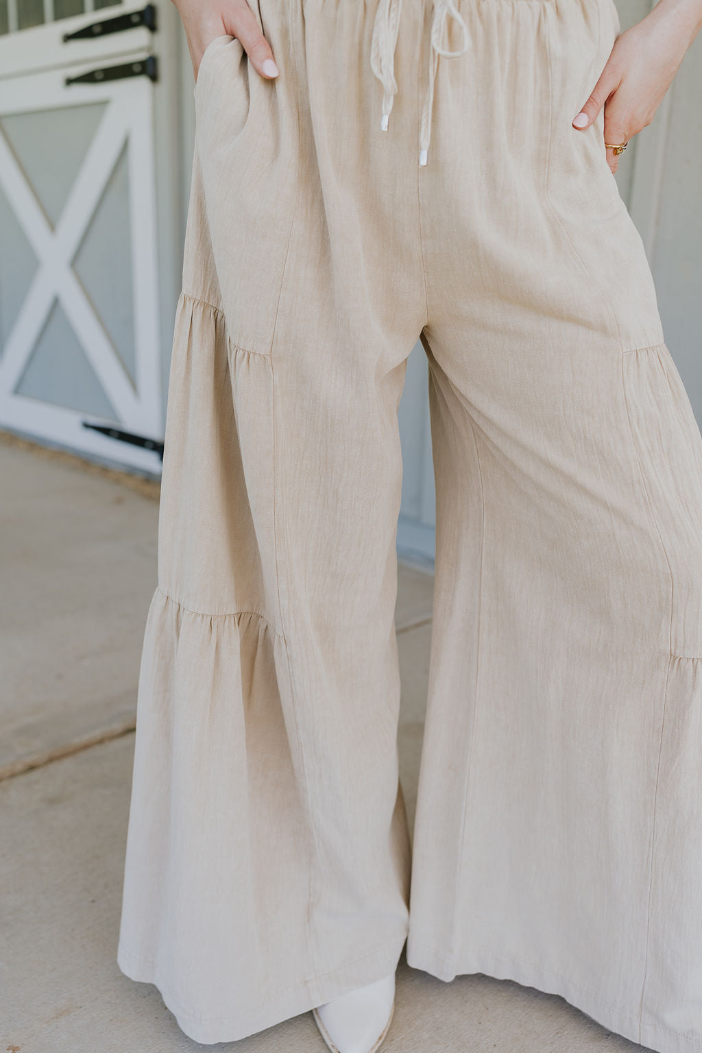 Close up front view of female model wearing the Carissa Washed Taupe Tiered Flare Pants which features Washed Taupe Cotton Fabric, Side Tiered Design, Flare Pants, Elastic Waistband with Drawstring Tie and Side Pockets