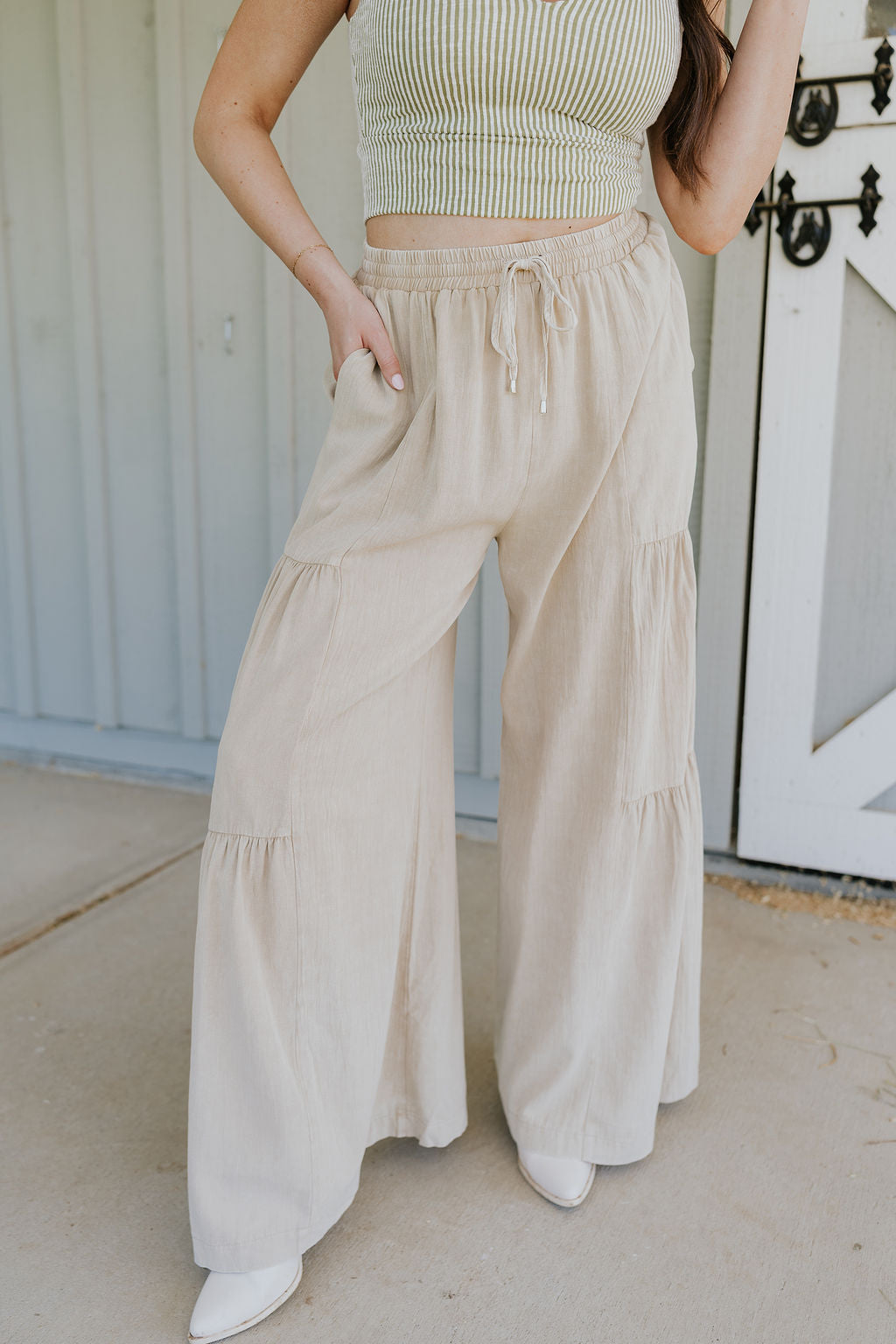 Front view of female model wearing the Carissa Washed Taupe Tiered Flare Pants which features Washed Taupe Cotton Fabric, Side Tiered Design, Flare Pants, Elastic Waistband with Drawstring Tie and Side Pockets