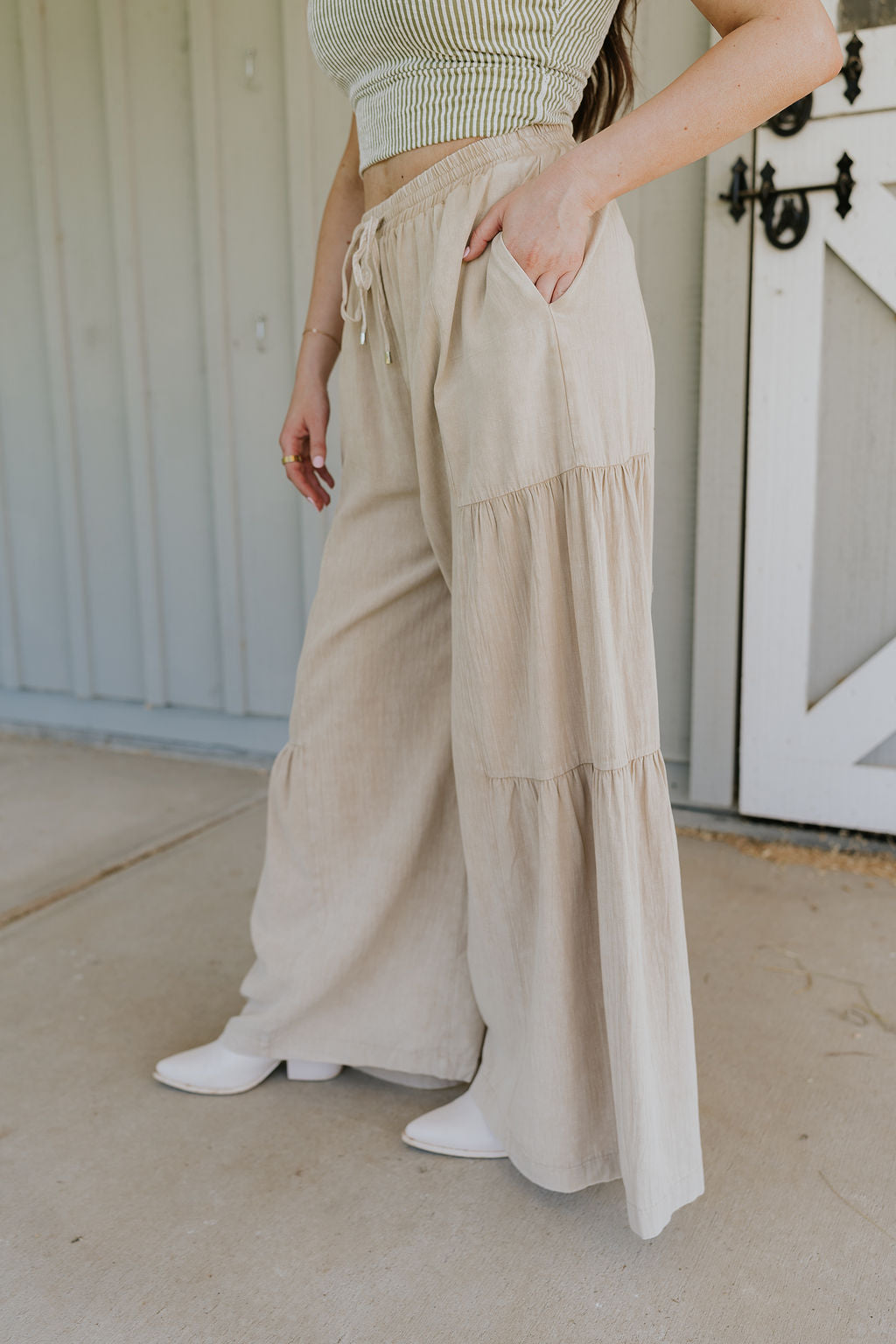 Side view of female model wearing the Carissa Washed Taupe Tiered Flare Pants which features Washed Taupe Cotton Fabric, Side Tiered Design, Flare Pants, Elastic Waistband with Drawstring Tie and Side Pockets