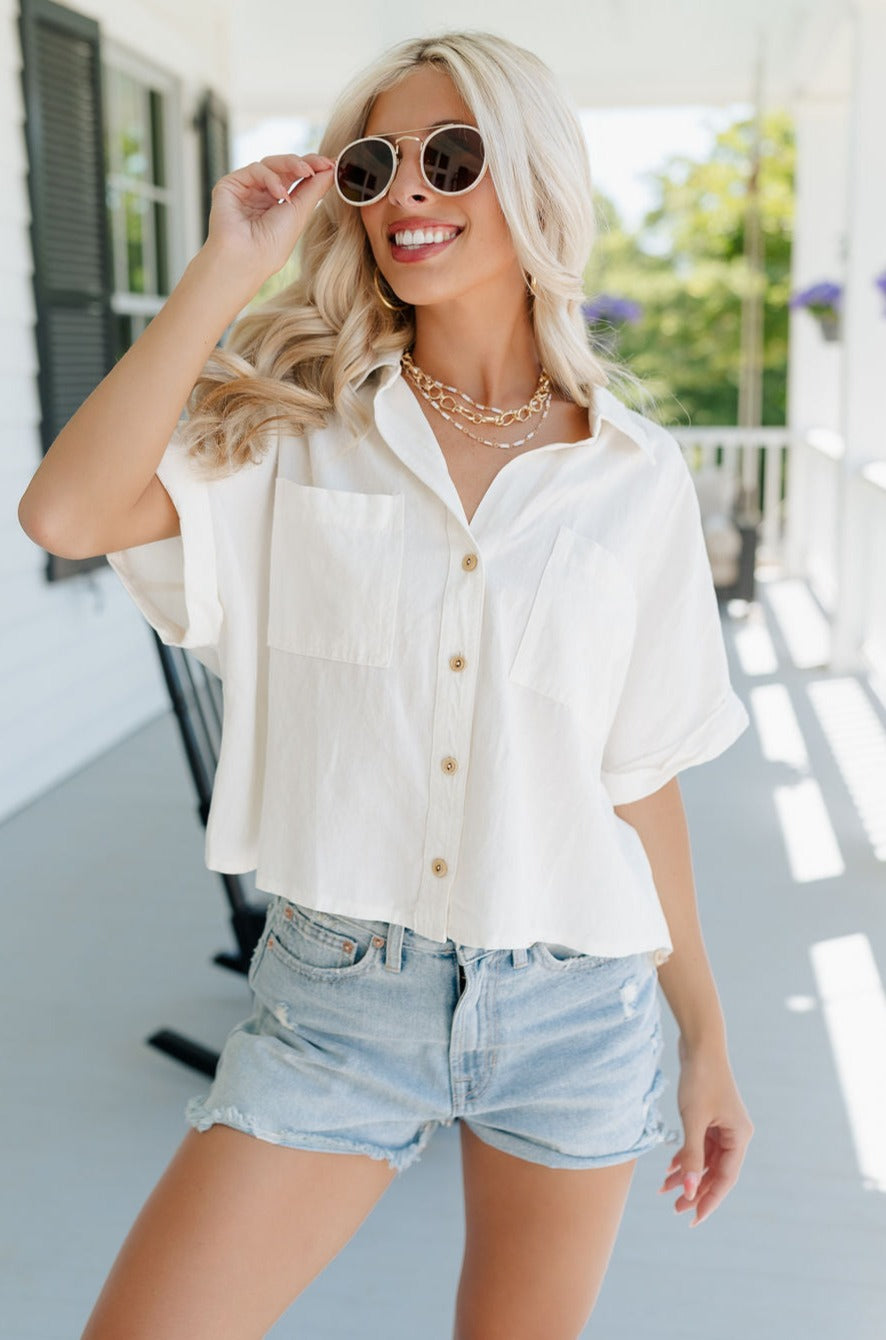 Front view of female model wearing the Cora White Short Sleeve Button-Up Top which features Off White Linen Fabric, Wooden Button Up Front Closure, Collared Neckline, Short Sleeves and Front Chest 