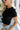 Close up side view of blonde model wearing the Kira Short Sleeve Cropped Top in Black that has black fabric. short sleeves, a round neck, and cropped waist. Worn with denim shorts.