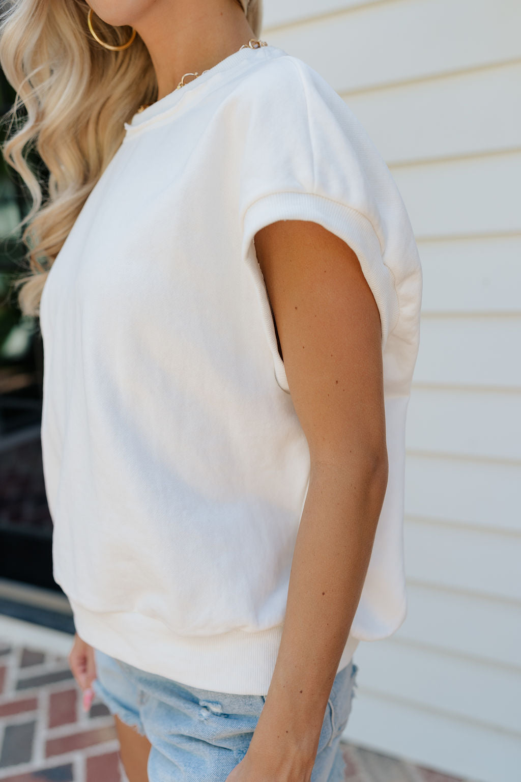 Close up side view of female model wearing the Ivy Cream Sleeveless Top which features White Cotton Fabric, Raw Thread Hem Details, Sleeveless andRound Neckline.