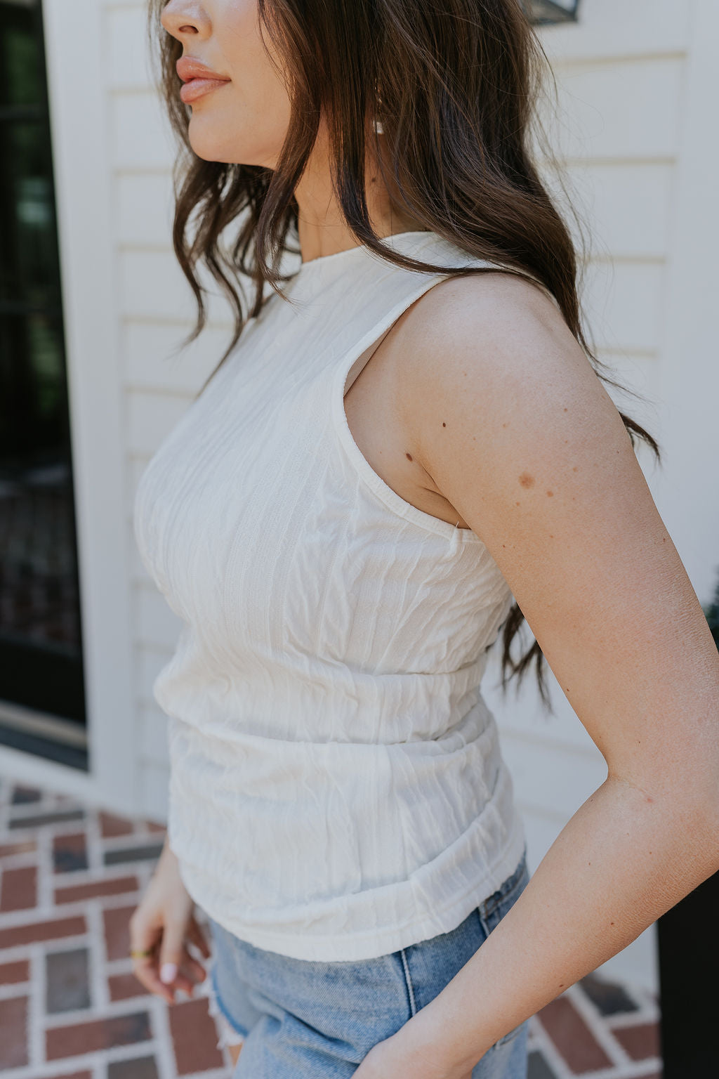Side view of female model wearing the Clara Cream Textured Sleeveless Tank which features Cream Texture Fabric, Round Neckline and Sleeveless