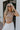 Upper body front view of blonde model wearing the Kira Short Sleeve Cropped Top in Taupe that has taupe fabric, short sleeves, a round neck, and cropped waist. Worn with white pants.