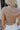 Close-up upper body back view of blonde model wearing the Kira Short Sleeve Cropped Top in Taupe that has taupe fabric, short sleeves, a round neck, and cropped waist. Worn with white pants.