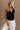 Front view of female model wearing the Jasmine Black Button-Up Vest which features Black Linen Fabric, Monochrome Button Up Front Closure, Cropped Waist, V-Neckline and Sleeveless