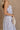 Side view of female model wearing the Cali Purple Floral Maxi Dress which features Sheer purple fabric, Purple floral print and white floral embroidery, Purple lining, Bustier top, Adjustable straps, Open back with a tie closure and elastic waist and Tiered skirt