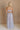 Full body back view of female model wearing the Cali Purple Floral Maxi Dress which features Sheer purple fabric, Purple floral print and white floral embroidery, Purple lining, Bustier top, Adjustable straps, Open back with a tie closure and elastic waist and Tiered skirt