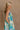 Side view of female model wearing the Mallory Green Multi Floral Sleeveless Midi Dress which features Green, blue, white, and yellow floral print, Round neckline, Adjustable straps, Keyhole back with tie closure and White lining
