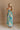 Back view of female model wearing the Mallory Green Multi Floral Sleeveless Midi Dress which features Green, blue, white, and yellow floral print, Round neckline, Adjustable straps, Keyhole back with tie closure and White lining