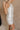 Side view of female model wearing the Isla White Silver Ruched Halter Neckline Mini Dress which features White Silver Fabric, White Lining, Ruched Details, Overlap Hem, Halter Neckline and Monochrome Back Zipper with Hook Closure
