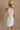 Back view of female model wearing the Isla White Silver Ruched Halter Neckline Mini Dress which features White Silver Fabric, White Lining, Ruched Details, Overlap Hem, Halter Neckline and Monochrome Back Zipper with Hook Closure