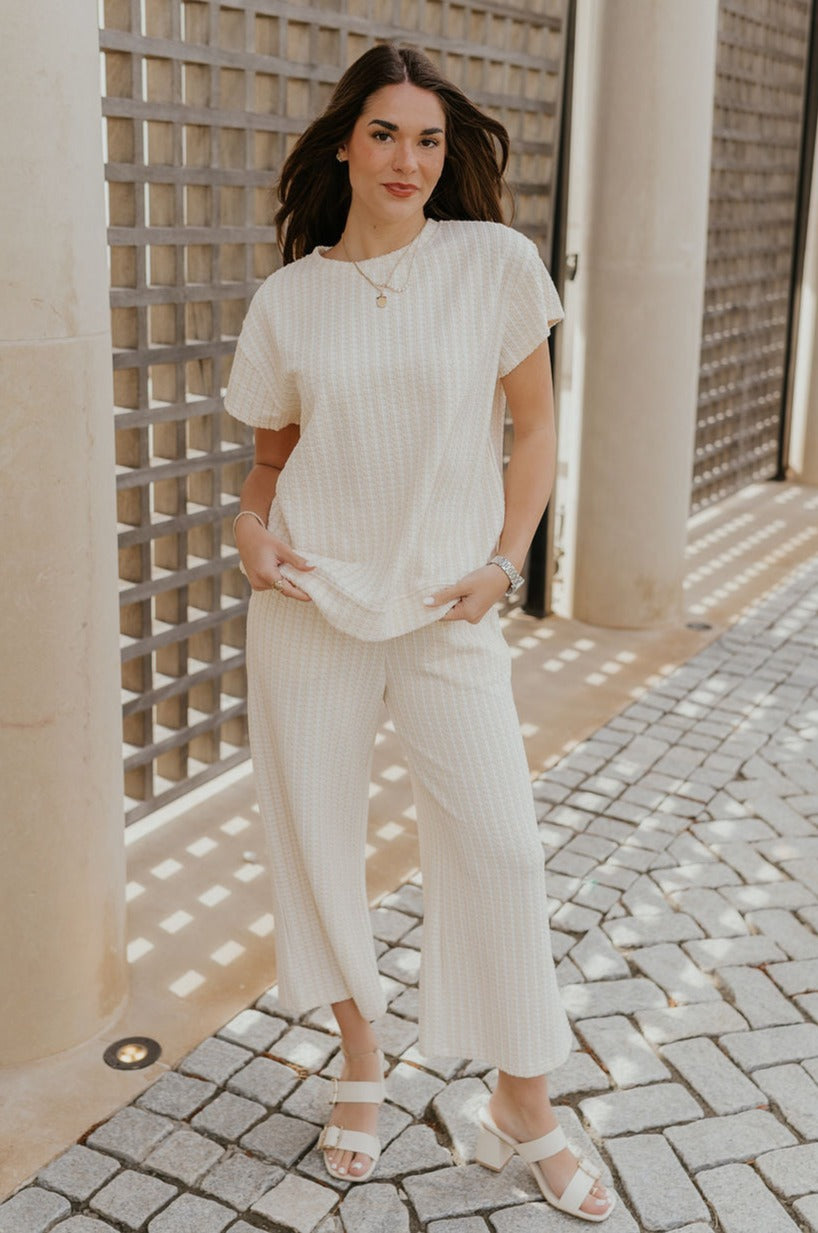 Full body view of female model wearing the Willow Cream Woven Short Sleeve Top which features Cream and White Woven Design, Thick Hem, Round Neckline and Short Sleeves