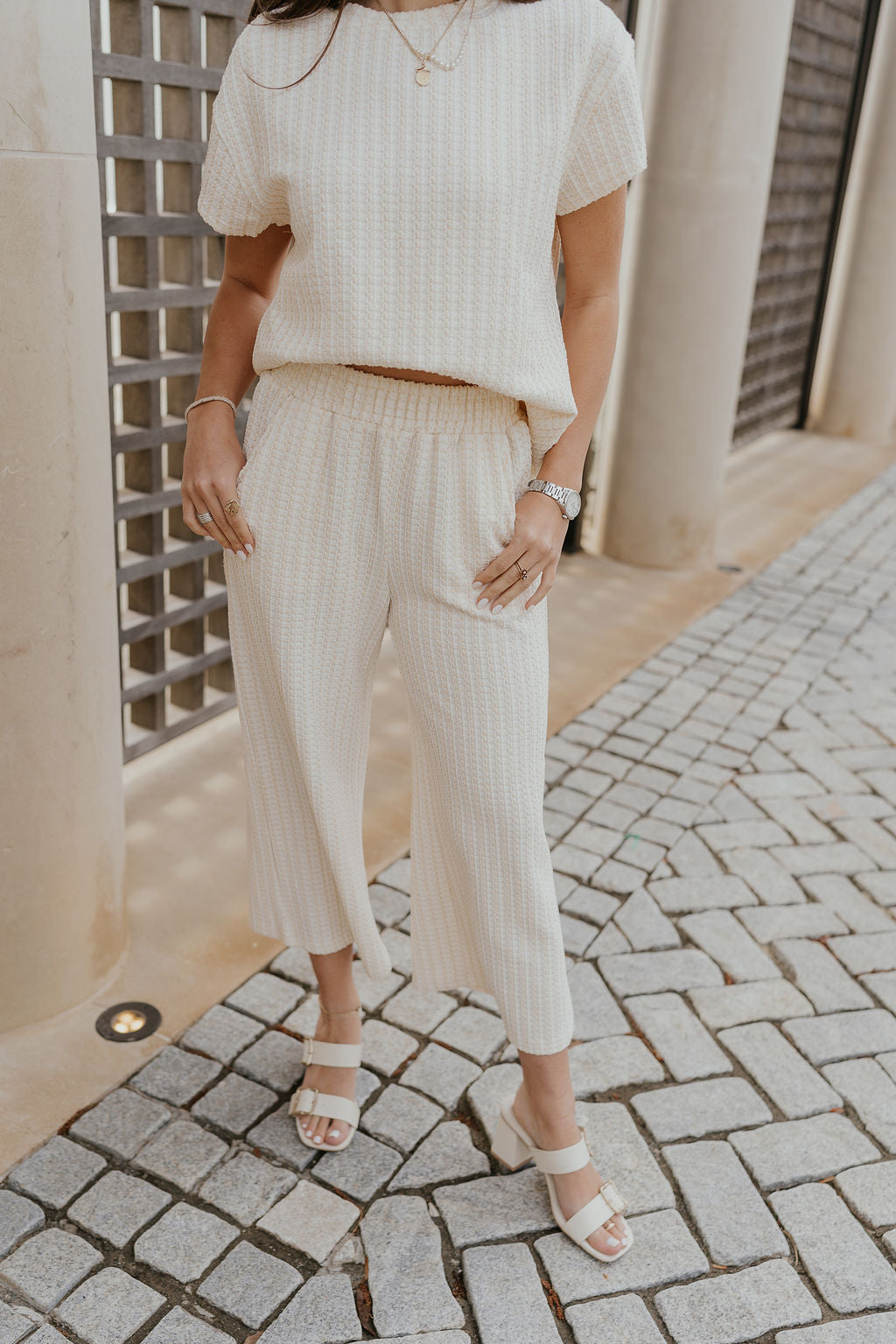 Front view of female model wearing the Willow Cream Woven Cropped Pants which features Cream and White Woven Design, Cropped Wide Pant Legs, Two Pockets On Each Side and Elastic Waistband