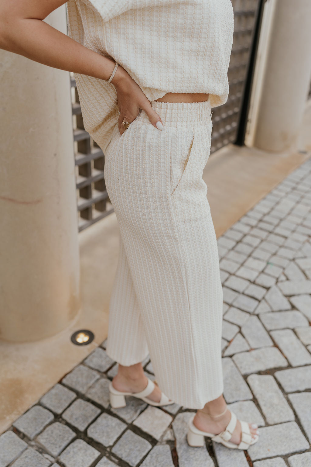 Close up side view of female model wearing the Willow Cream Woven Cropped Pants which features Cream and White Woven Design, Cropped Wide Pant Legs, Two Pockets On Each Side and Elastic Waistband