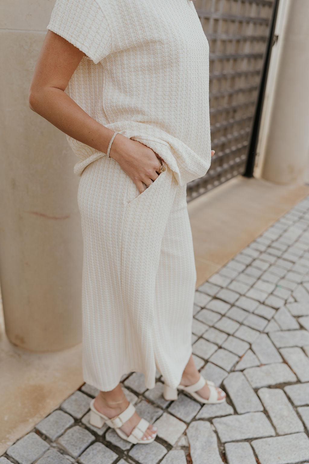 Close up side view of female model wearing the Willow Cream Woven Cropped Pants which features Cream and White Woven Design, Cropped Wide Pant Legs, Two Pockets On Each Side and Elastic Waistband