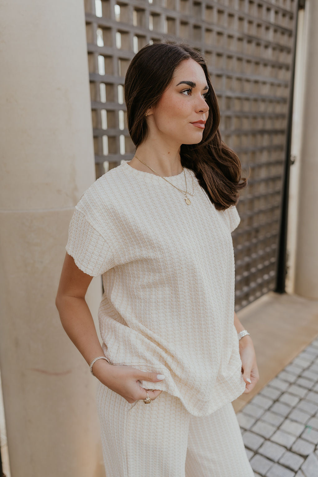 Side view of female model wearing the Willow Cream Woven Short Sleeve Top which features Cream and White Woven Design, Thick Hem, Round Neckline and Short Sleeves