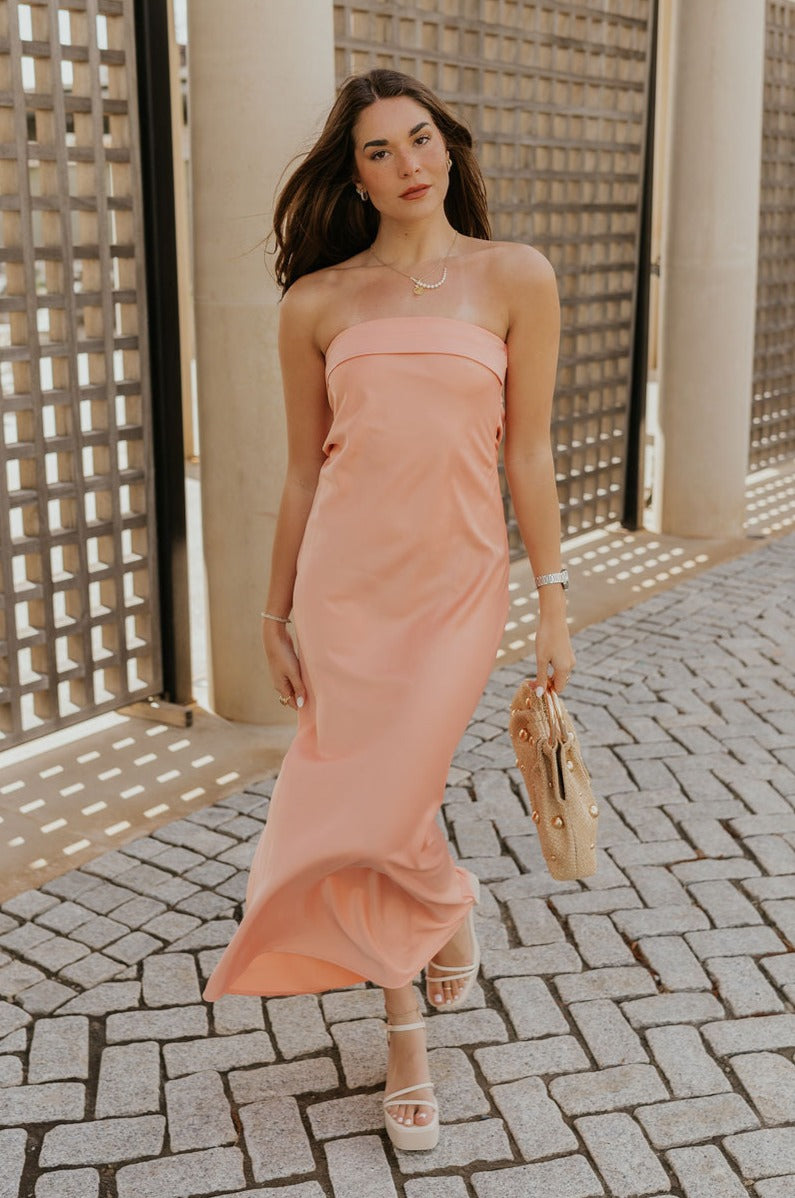 Full body view of female model wearing the Lyla Peach Satin Midi Dress which features Peach Satin Fabric, Maxi Length, Strapless Design, Back Cut-Out Design and Monochrome Side Zipper with Hook Closure