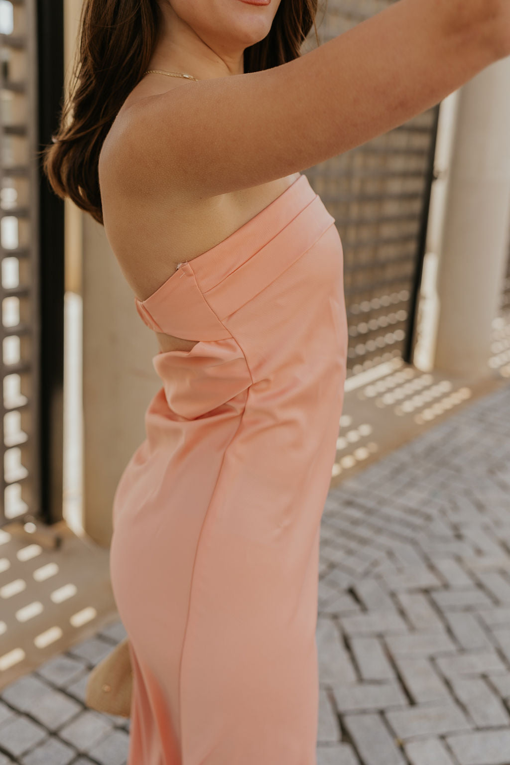 Close up side view of female model wearing the Lyla Peach Satin Midi Dress which features Peach Satin Fabric, Maxi Length, Strapless Design, Back Cut-Out Design and Monochrome Side Zipper with Hook Closure