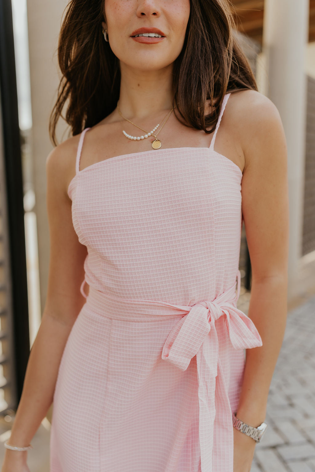 Close up view of female model wearing the Valeria Baby Pink Tie Mini Dress which features Light Pink Lightweight Fabric, Monochrome Micro Plaid Pattern, Light Pink Lining, Mini Length, Tie Waistband, Square Neckline, Adjustable Straps and Back Zipper with Hook Closure