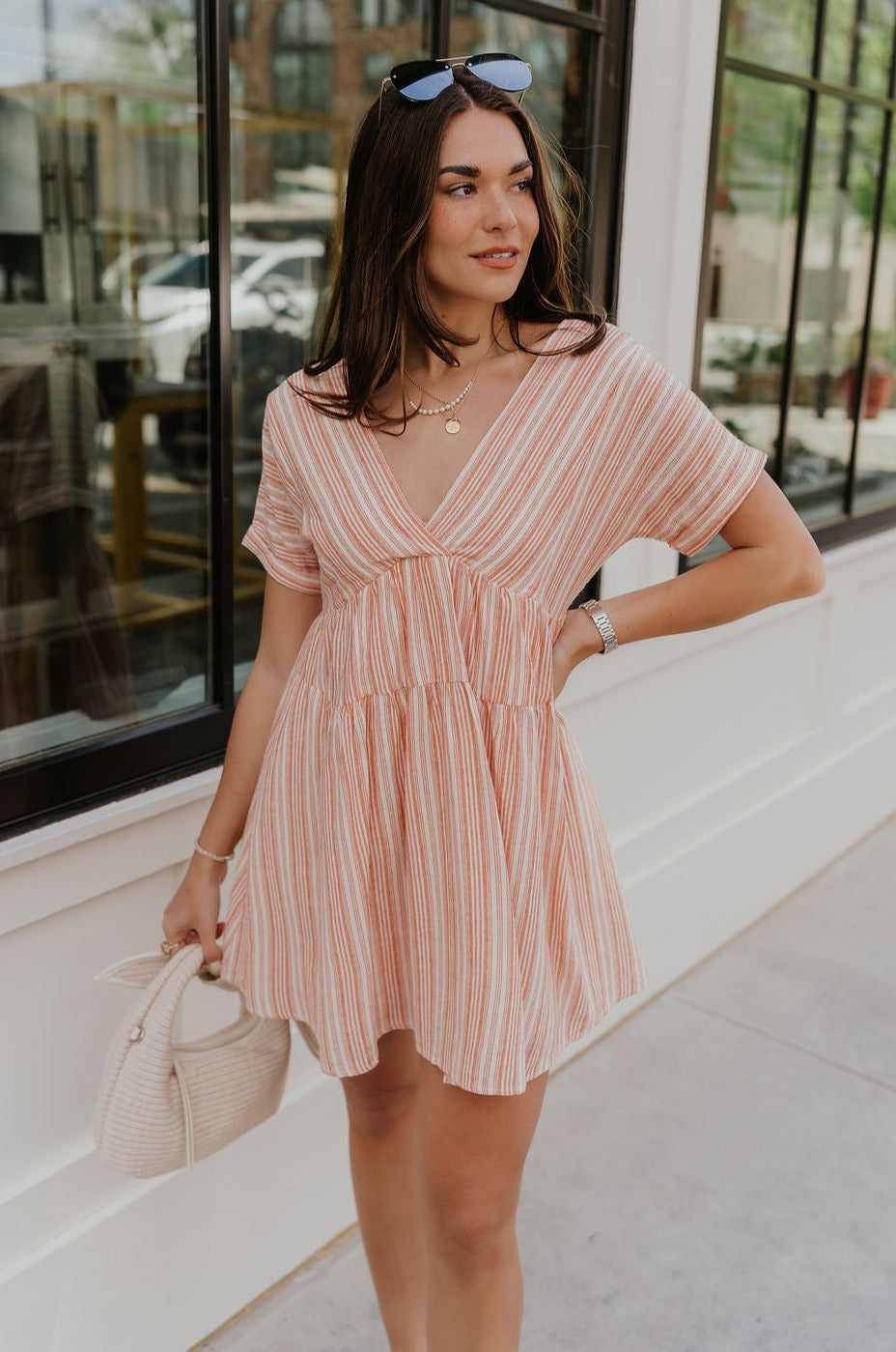 Front view of female model wearing the Brynlee Sunkist Orange & Cream Stripe Mini Dress which features orange and Cream Stripe Pattern, Mini Length, Cream Lining, Pockets on each side, Plunge Neckline, Short Sleeves and Back Tie Closure