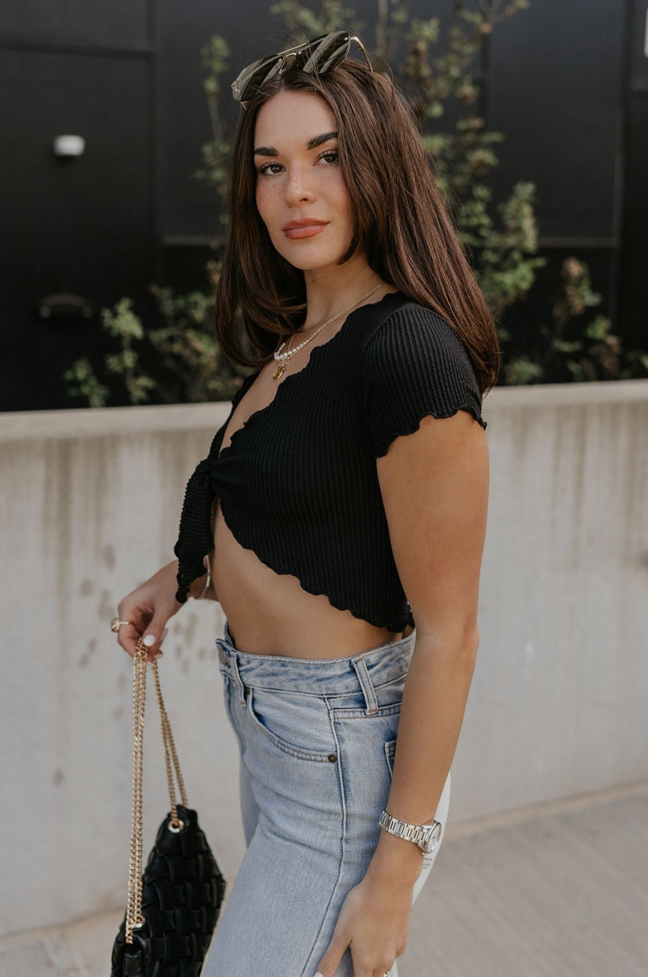 Side view of female model wearing the Daphne Black Lettuce Crop Tie Top which features Black Ribbed Fabric, Lettuce Hem Details, Cropped Waist, Front Tie Detail and Short Sleeves