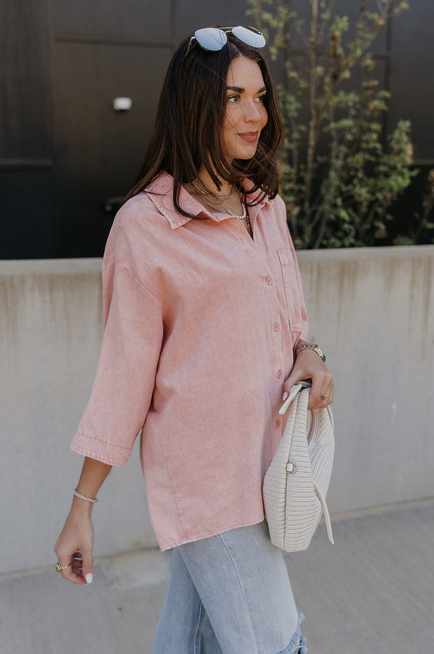 Side view of female model wearing the Ezra Soft Pink Button-Up Top which features Muted Pink Cotton Fabric, Monochrome Front Button Up Closure, Front Left Chest Pocket, Collared Neckline and Short Sleeves