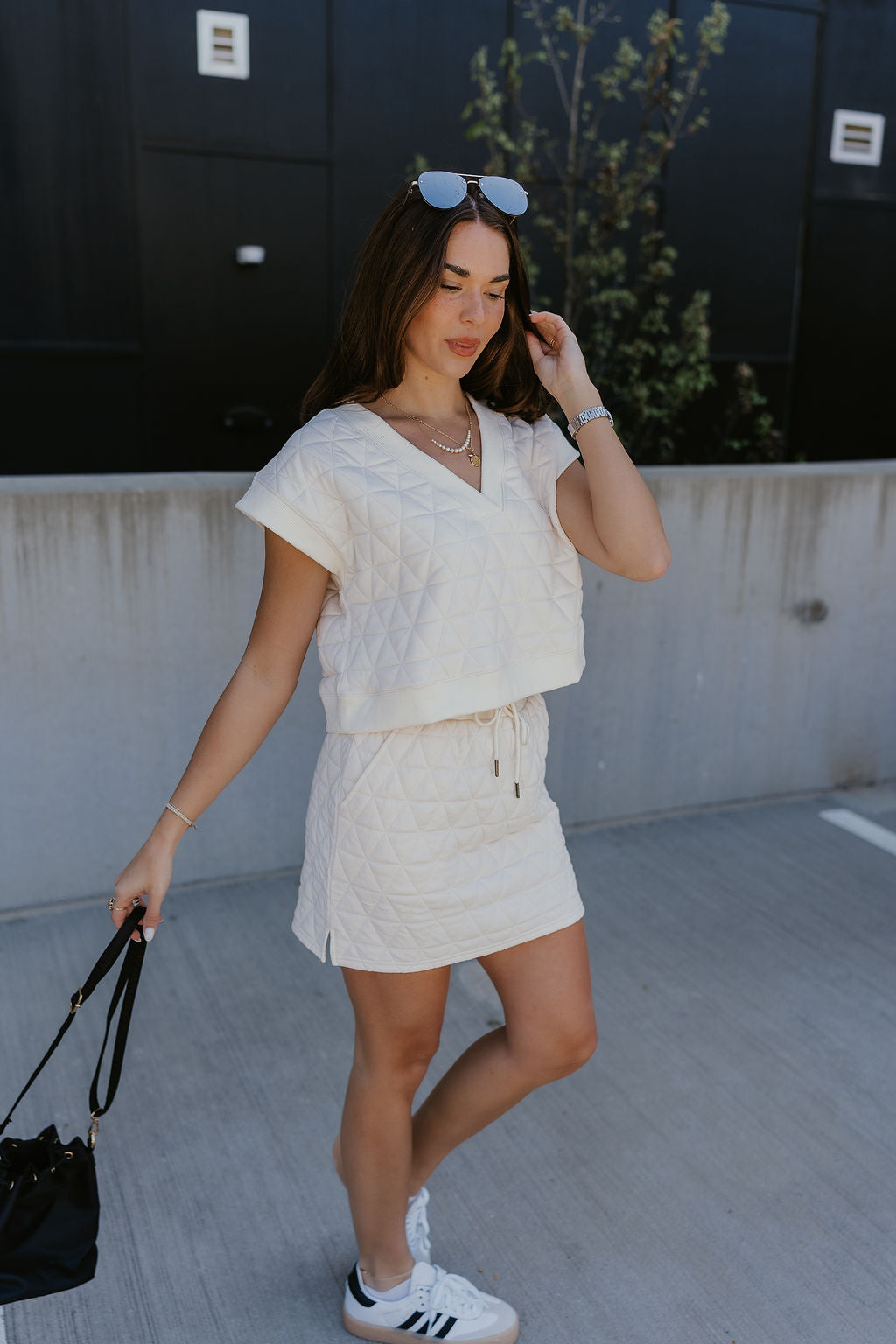 Full body side view of female model wearing the Berkley Cream Quilted Short Sleeve Top that has cream quilted fabric, a v-neck and short sleeves. Worn with matching skirt.