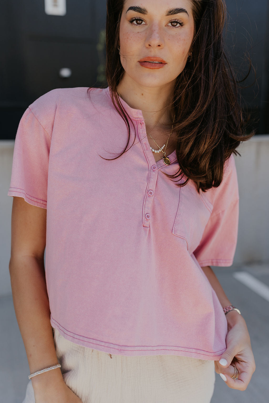 Close Front view of model wearing the Elise Pink Cropped Short Sleeve Tee that has pink knit fabric, a button up neckline, a chest pocket, and short sleeves.