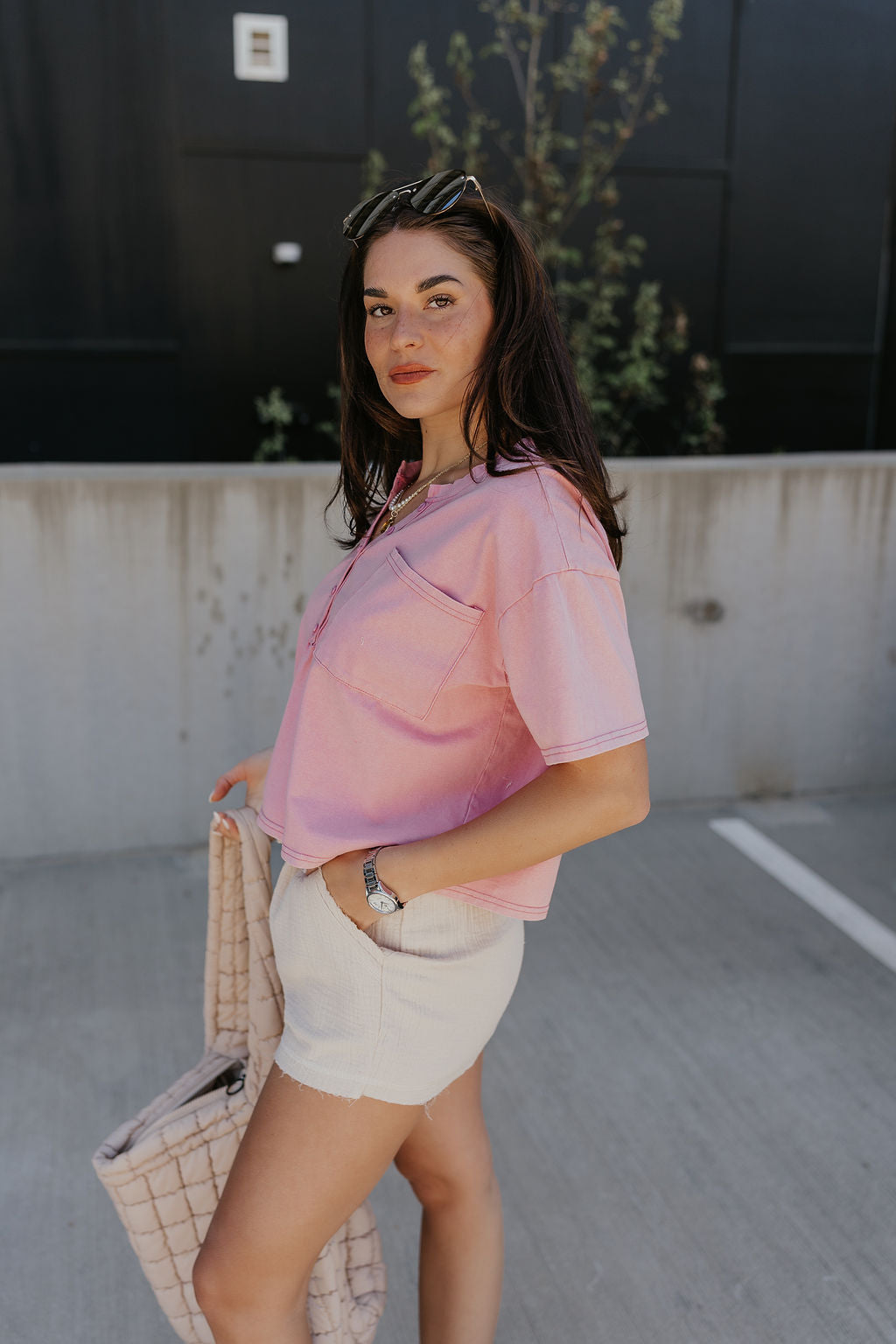 Side view of model wearing the Elise Pink Cropped Short Sleeve Tee that has pink knit fabric, a button up neckline, a chest pocket, and short sleeves.