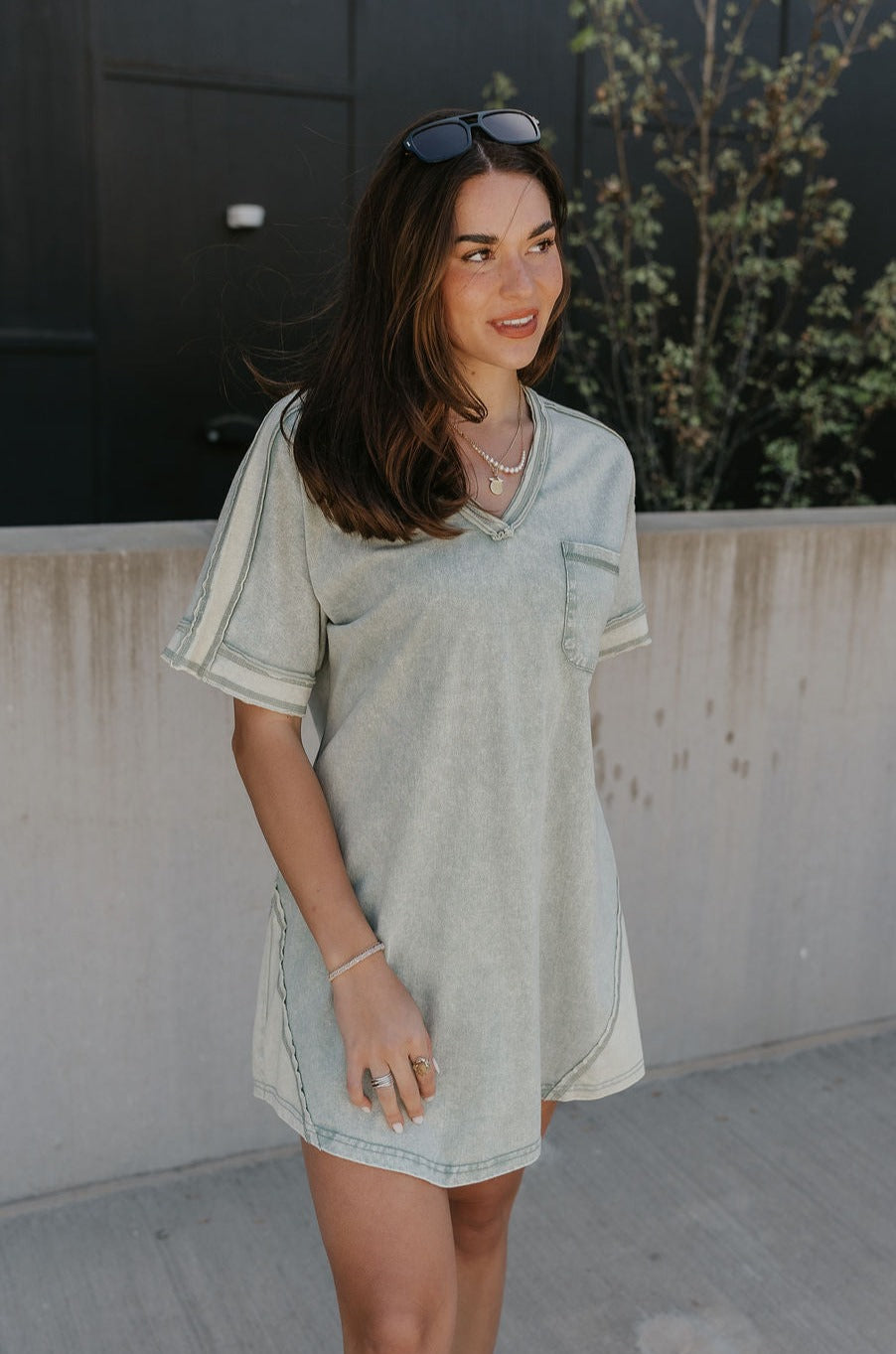 Upper body front view of female model wearing the Dalia Sage Green Knit Mini Dress that has washed sage green fabric, a front pocket, and short sleeves.