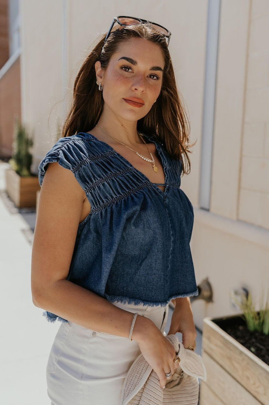Side view of female model wearing the Chloe Medium Denim Fray Sleeveless Top which features Medium Denim Blue Fabric, Fray Hem, Upper Ruched Details, V-Neckline and Sleeveless
