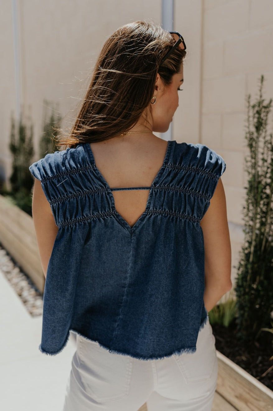 Back view of female model wearing the Chloe Medium Denim Fray Sleeveless Top which features Medium Denim Blue Fabric, Fray Hem, Upper Ruched Details, V-Neckline and Sleeveless