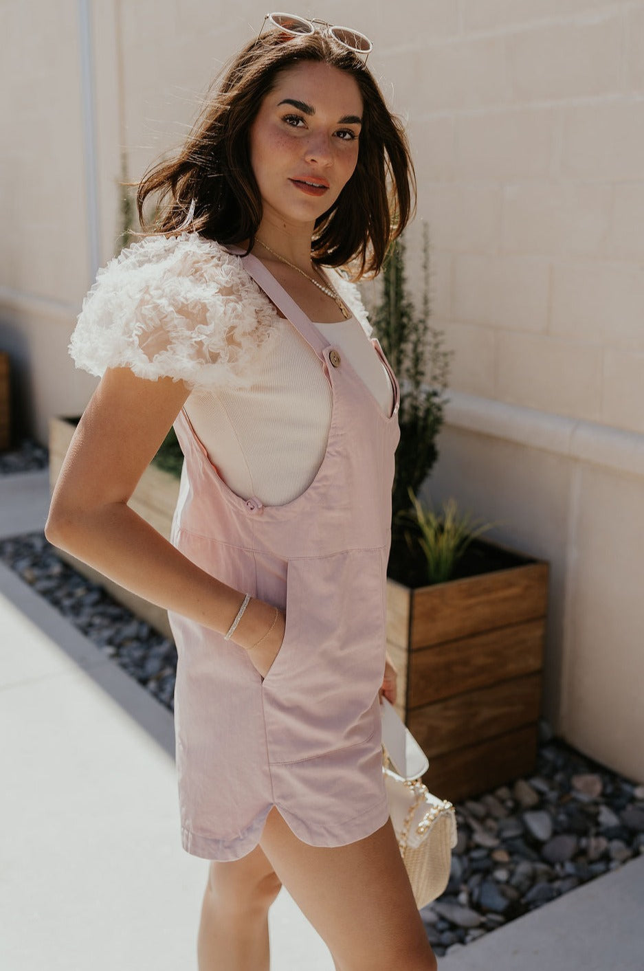 Side view of female model wearing the Selah Mauve Pink Sleeveless Romper which features Mauve Pink Lightweight Fabric, Pockets On Each Side, Slight Slit Details, Scoop Neckline, Straps with Wooden Button Closures and Sleeveless