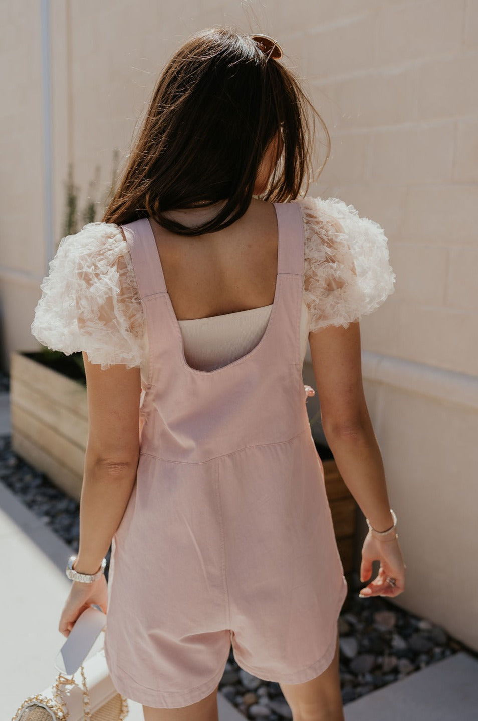 Back view of female model wearing the Selah Mauve Pink Sleeveless Romper which features Mauve Pink Lightweight Fabric, Pockets On Each Side, Slight Slit Details, Scoop Neckline, Straps with Wooden Button Closures and Sleeveless