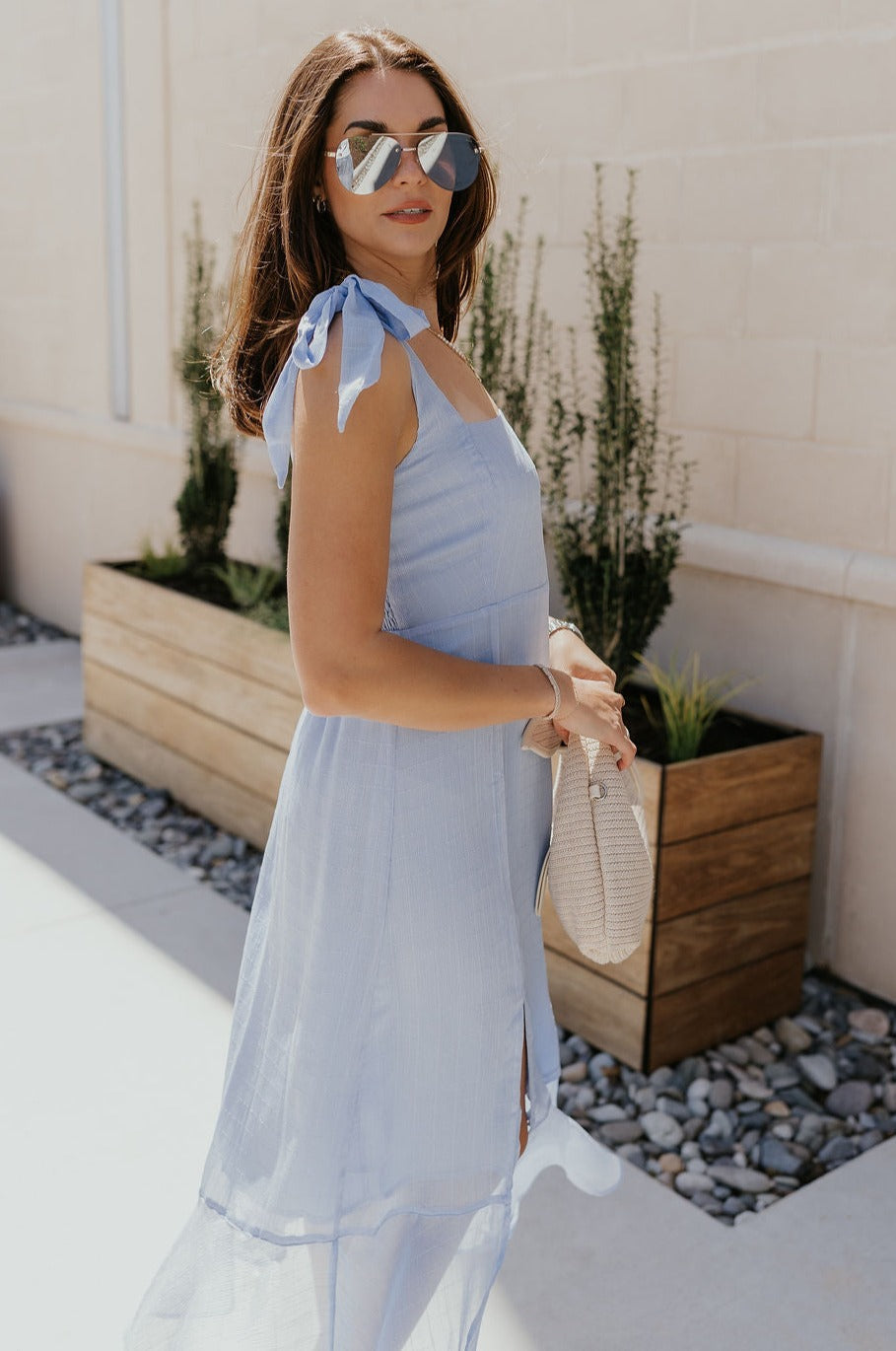 Side view of female model wearing the Laurel Light Blue Slit Midi Dress which features Light Blue Lightweight Fabric, Ruffle Hem, Light Blue Lining, Midi Length, Textured Details, Square Neckline and Tie Straps