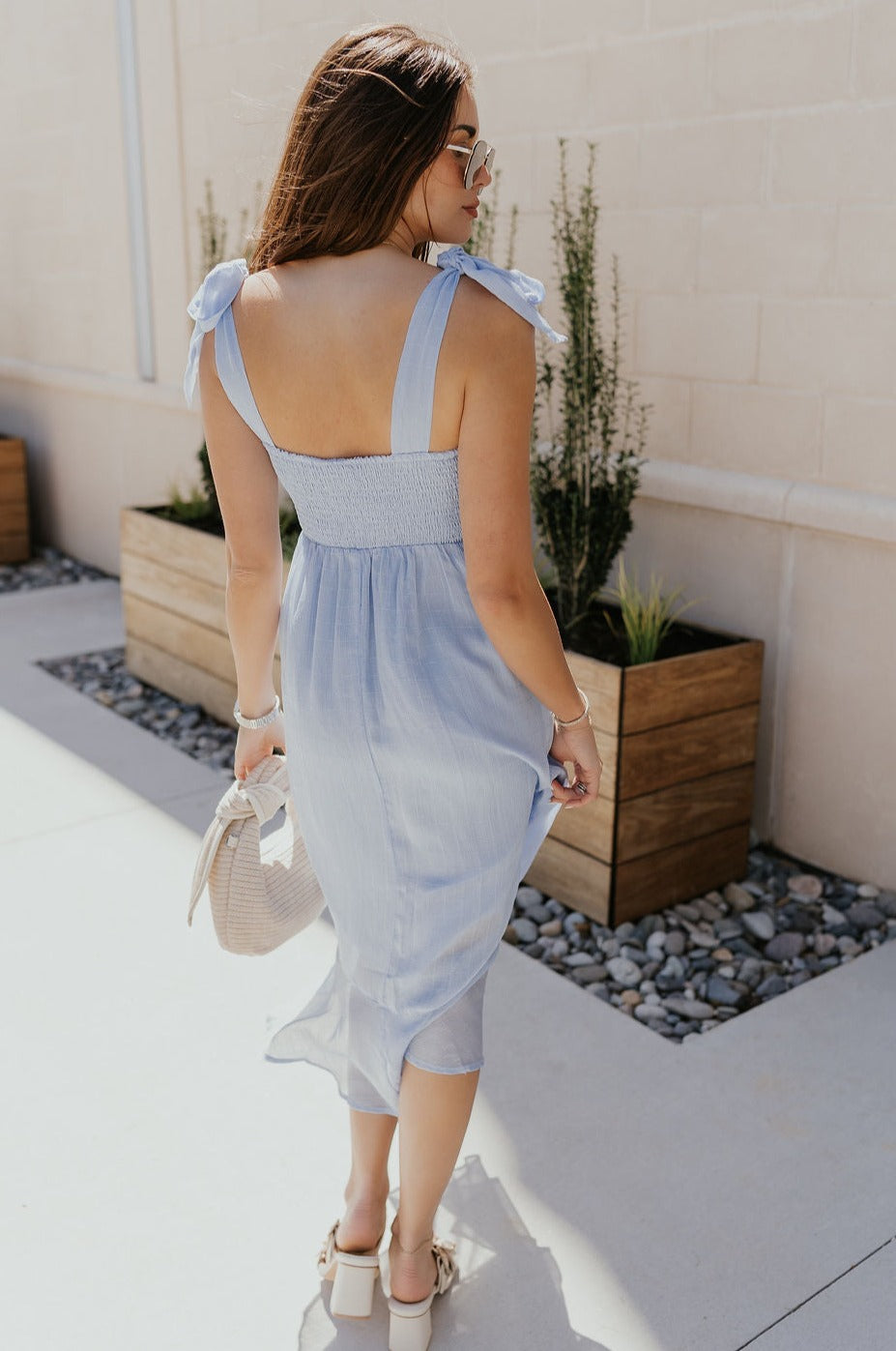 Full body back view of female model wearing the Laurel Light Blue Slit Midi Dress which features Light Blue Lightweight Fabric, Ruffle Hem, Light Blue Lining, Midi Length, Textured Details, Square Neckline and Tie Straps