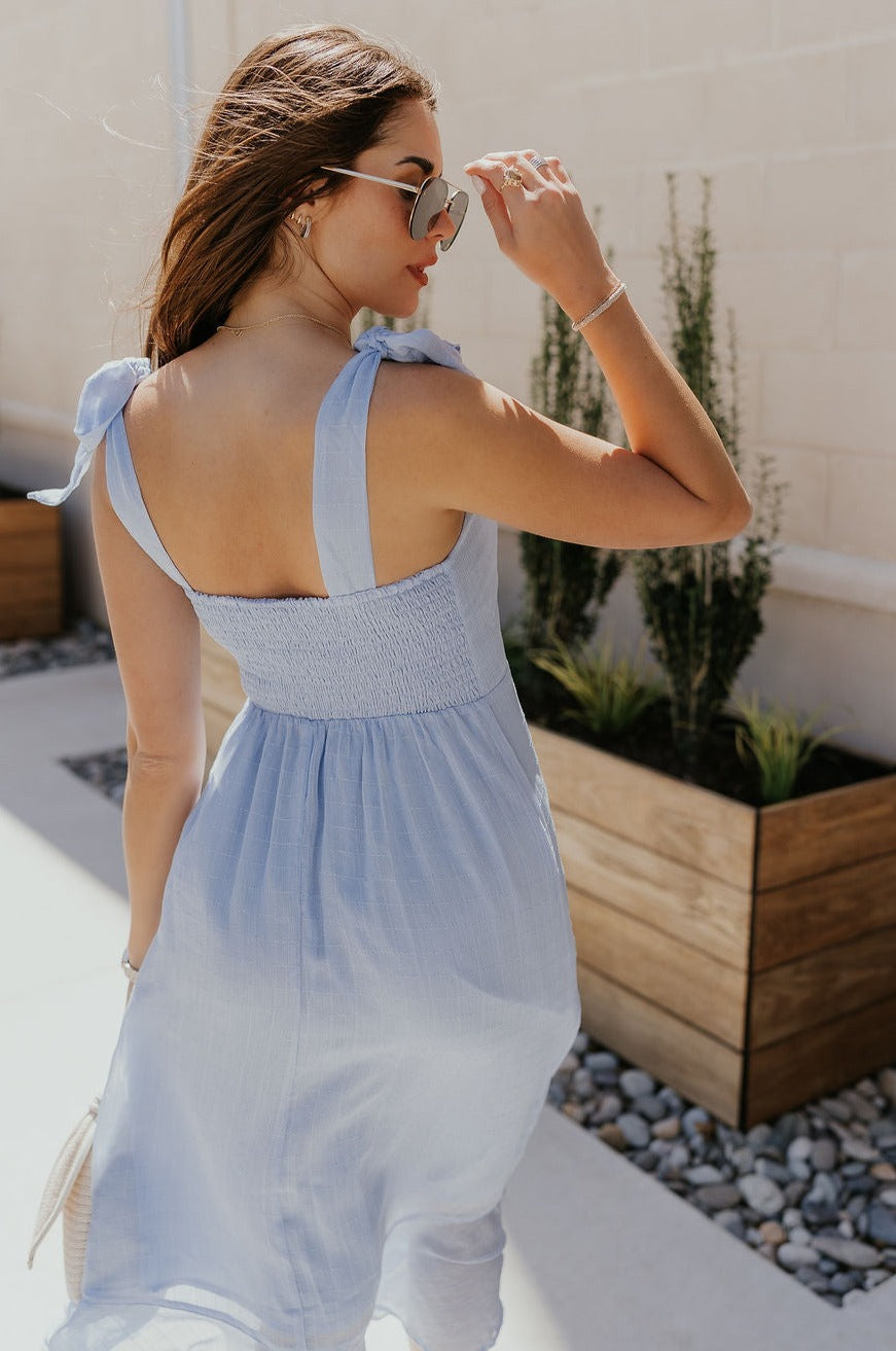 Back view of female model wearing the Laurel Light Blue Slit Midi Dress which features Light Blue Lightweight Fabric, Ruffle Hem, Light Blue Lining, Midi Length, Textured Details, Square Neckline and Tie Straps