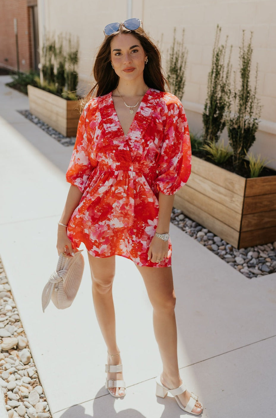 Full body front view of female model wearing the Brittany Red & Pink Floral Mini Dress that has red and pink floral print, a plunge neck, elastic waist, and puff sleeves.
