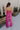 Full body back view of female model wearing the Baylee Magenta Convertible Jumpsuit that has magento fabric, wide legs, and a neckline that can be halter or a front tie. Shown as halter.