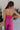 Upper body back view of female model wearing the Baylee Magenta Convertible Jumpsuit that has magento fabric, wide legs, and a neckline that can be halter or a front tie. Shown as halter.