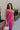 Upper body front view of female model wearing the Baylee Magenta Convertible Jumpsuit that has magento fabric, wide legs, and a neckline that can be halter or a front tie. Shown as strapless.