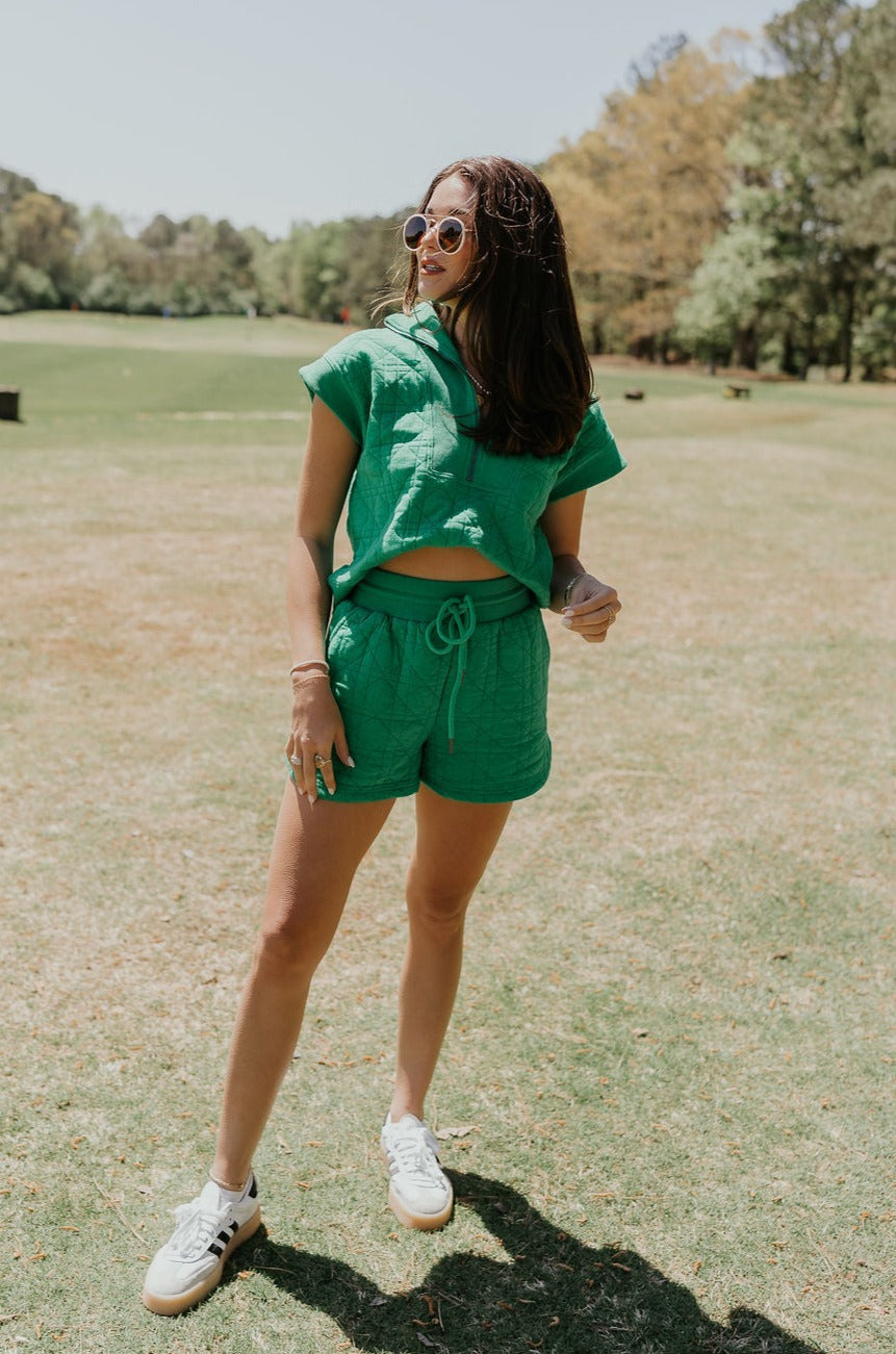 Full body front view of female model wearing the Paulina Green Quilted Shorts that have green quilted fabric, a drawstring elastic waist, and side pockets. Worn with matching top